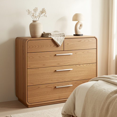 Commode Sirius en bois clair aux lignes arrondies, intégrée dans une chambre contemporaine lumineuse avec des accessoires décoratifs sobres.